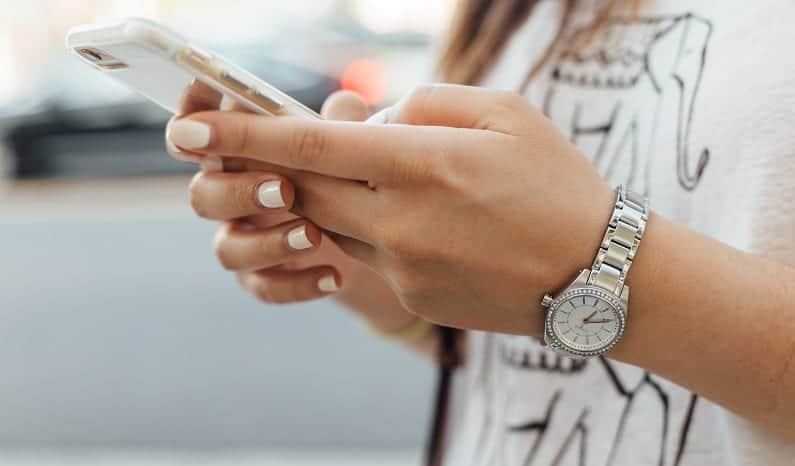 Na imagem, há a mão de uma menina segurando um celular. Um detalhe que chama a atenção é que ela também utiliza um relógio na sua mão esquerda.