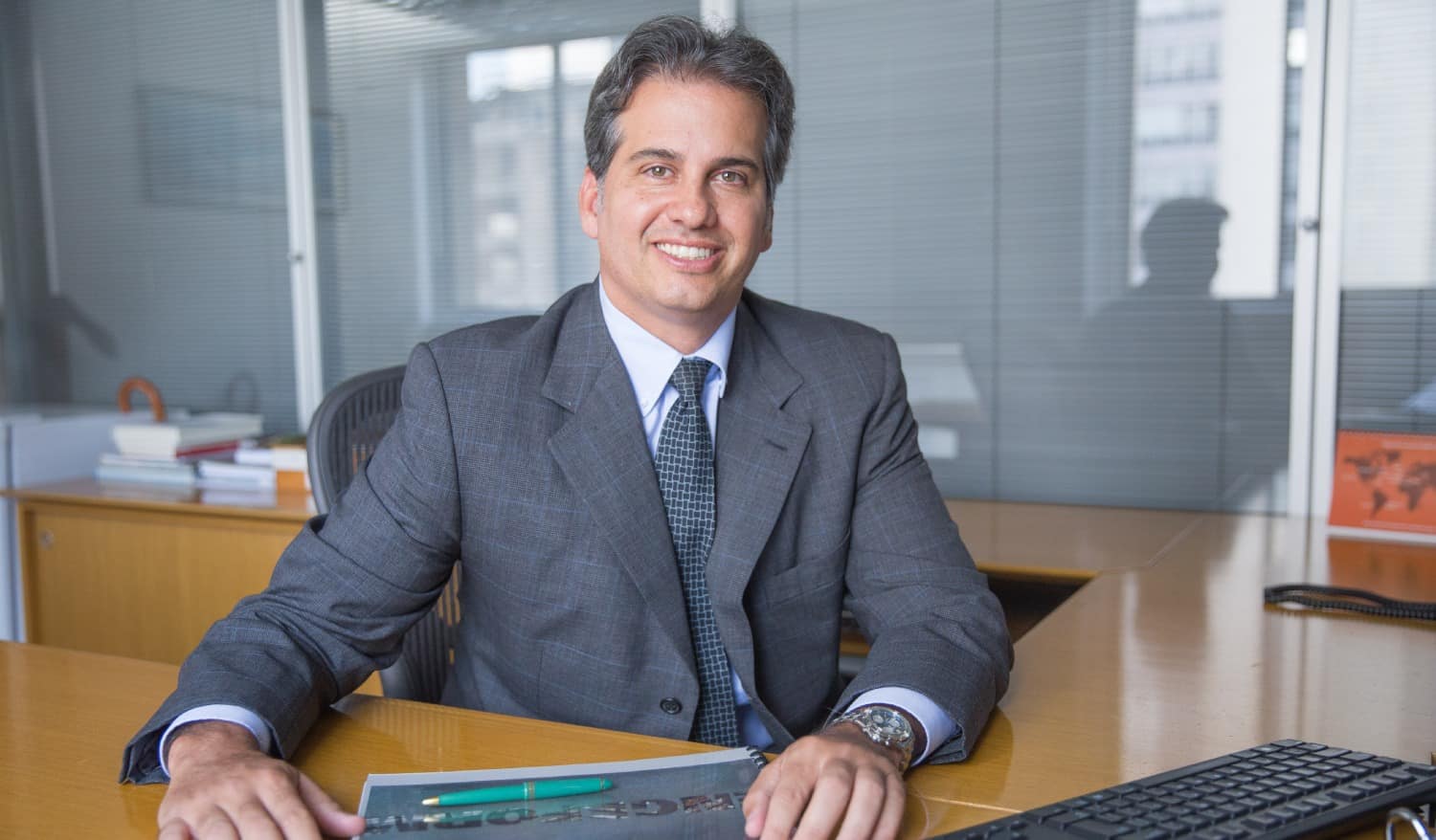 A imagem é uma foto do executivo André Abucham, CEO da empresa Engeform. Ele está usando terno social cinza e está sentado em uma mesa de escritório com as mãos recostadas.
