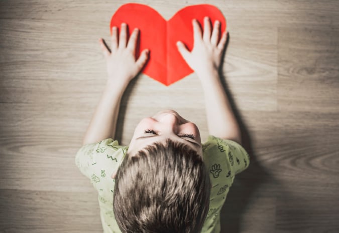 Na foto, uma criança se apoia no desenho de coração vermelho no chão