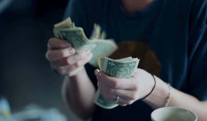 A imagem mostra as mãos de uma mulher contando notas de dólar