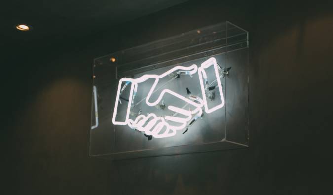 A imagem mostra luzes de neon em formato de um aperto de mão